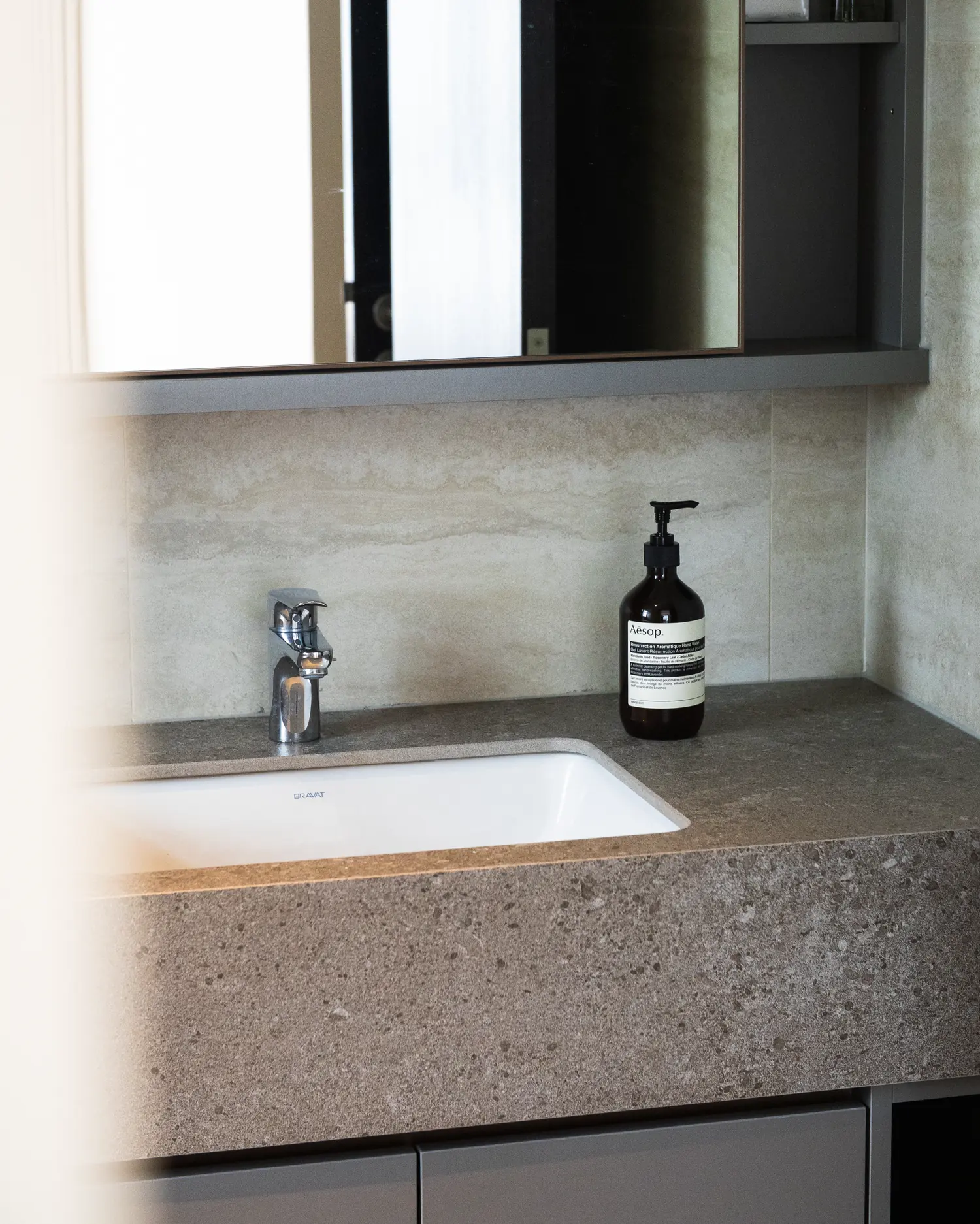 The bathroom, travertine-toned tiling with a speckled stone vanity